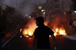 Anti-Fascist protester with burning building in background. Photo Credit: The Associated Press, Kostas Tsironis